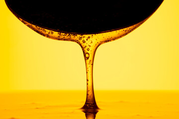 Honey dripping, pouring from dark spoon on yellow background. Thick viscous honey molasses flowing. Close up of golden honey liquid, sweet product of beekeeping. Sugar syrup is pouring. - obrazy, fototapety, plakaty
