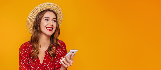 Young woman in a red summer dress, a straw hat with red lips holds a mobile phone, a smartphone in...
