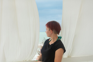 Fototapeta na wymiar Young woman with short hair looks at the sea in summer from hotel window