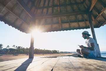 Relaxed and cheerful. Listening to music. Outdoor portrait of happy young african man resting on deck near the sea.