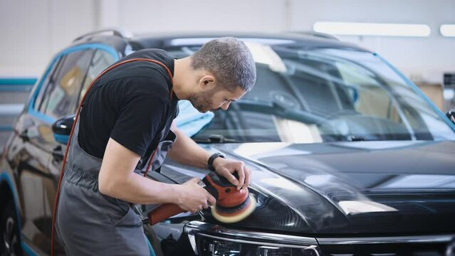 Cosmetic work with the appearance of the car. A man polishes the hood of a car in a ditying studio.