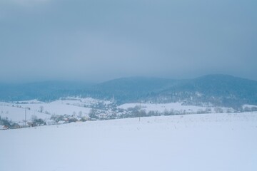 Fototapeta na wymiar Snowing landscape in Europe. Lonely small village before the storm at mountains
