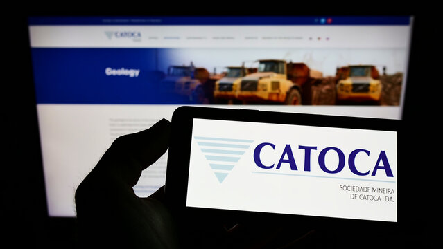 Stuttgart, Germany - 05-22-2022: Person holding cellphone with logo of mining company Sociedade Mineira de Catoca Lda. on screen in front of webpage. Focus on phone display.