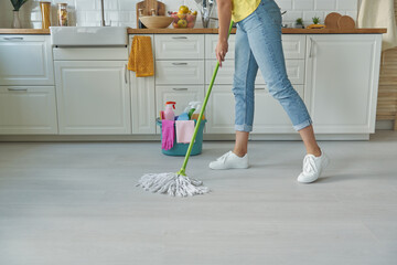 Close-up of woman cleaning floor with mop while standing at the domestic kitchen