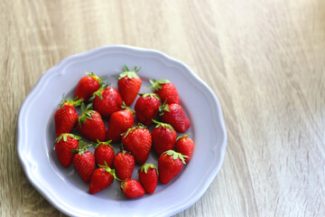Lilac plate full of fresh strawberries on wooden table. Selective focus.