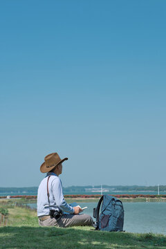A male tourist and photographer with a cowboy hat sits in the ecological Lakeside Park of Maoming open pit mine