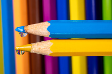 Blue and yellow pencils with drops of water on rods on the background of a set of colored pencils....
