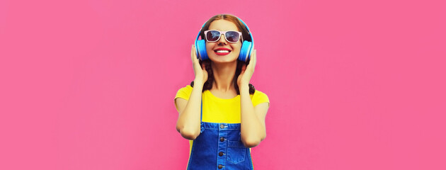 Portrait of happy smiling young woman with headphones listening to music on pink background, blank...