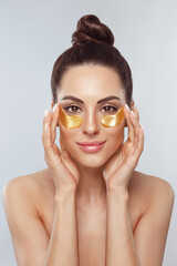 Beauty model girl face with healthy fresh skin. Woman with under eye collagen gold pads.  Skin care concept, anti-aging moisturizing eye mask, golden hydrogel patches, eye skin treatment, cosmetology.