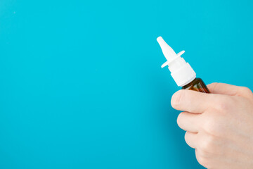 nasal spray in hand on a blue background with copy space, runny nose treatment, medicine and pharmacy, rhinitis medicines - obrazy, fototapety, plakaty