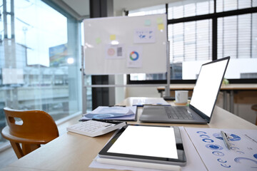 Laptop computer, digital tablet and financial documents on wooden table in board room