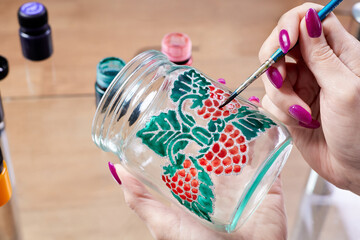 A girl paints a glass jar with stained glass paints