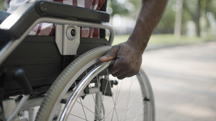Fototapeta na wymiar Hands of black man pushing wheel of wheelchair, life with disability in a city