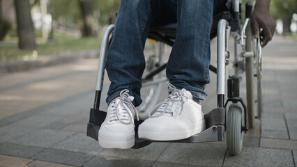 Person using manual wheelchair in park, physical disability, close-up of male feet