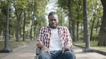 Obraz premium Upset man sitting in wheelchair in park, suffering from depression after injury
