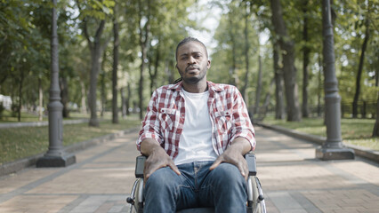 Young African-American man with disability sitting in wheelchair, looking seriously - obrazy, fototapety, plakaty