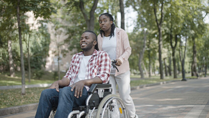 Young African woman pushing boyfriend's wheelchair, disability, partner's support