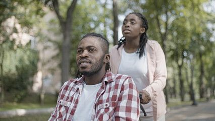 Caregiver pushing wheelchair with disabled man in park, surgery recovery care