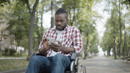 Black man in wheelchair using mobile application on smartphone, technology