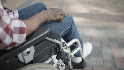 Close-up of person sitting in wheelchair in a park, rehabilitation after injury