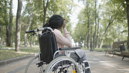 Fototapeta na wymiar African American woman with disability sitting in wheelchair in park, loneliness