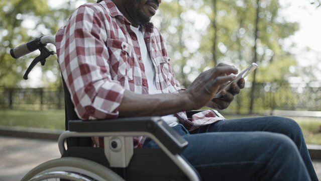 Male wheelchair user typing on smartphone, making online order in mobile app