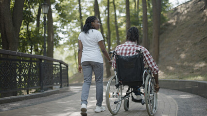 Woman holding boyfriend in wheelchair by hand in park, partner's support, back view