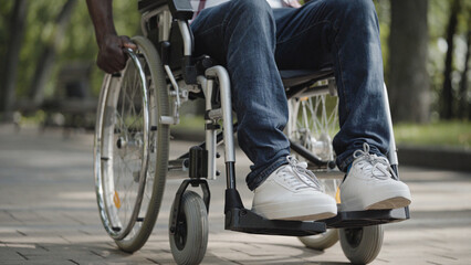 Obraz premium Man using wheelchair in city street, mobility impairment, living with disability, feet close-up