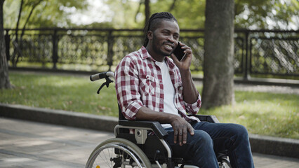 Happy man with disability using phone, talking to someone while sitting in wheelchair