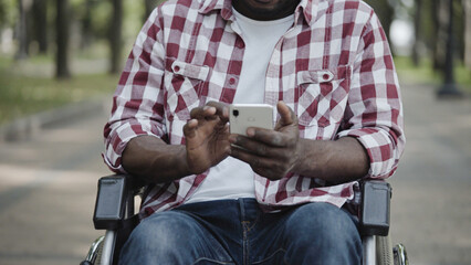 African American man with disability sitting in wheelchair, scrolling smartphone