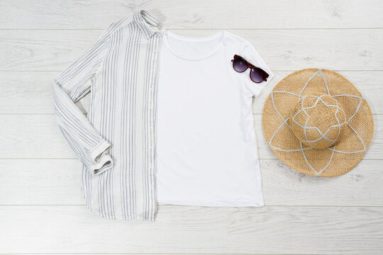 White closeup t shirt mock up flat lay on wooden background. Summer accessories. Hat, sunglasses. Top view and copy space. Mockup t-shirt and summertime. Template blank shirt.