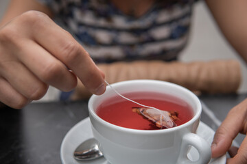 Woman's hands stirring the tea bag sitting in a coffee shop. Close-up of a hand stirring a portion of red tea in hot water inside a white cup. Lifestyle concept.