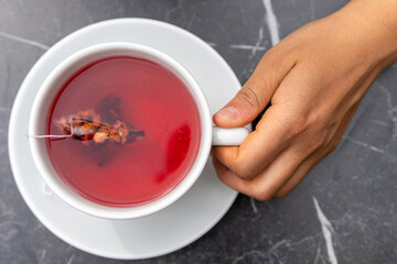 Woman's hand holding a cup of red tea by the handle. Close-up of a female hand holding a white cup...