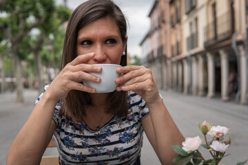 Brunette woman taking her white cup with both hands and sipping. Young girl with serious expression giving a drink or sip of her tea or coffee. Lifestyle concept.