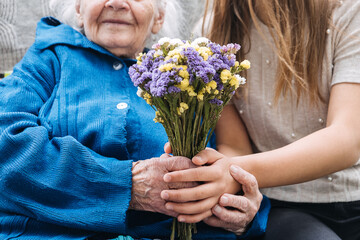 Volunteer girl and Senior elderly woman with gift, flowers bouquet and basket of groceries
