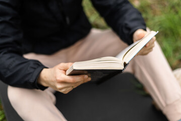 The woman is holding a book in her hands. Reading in the park, in the forest. Rest, training,...