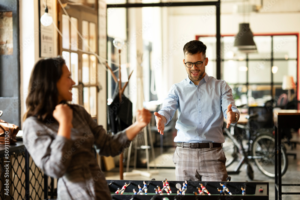 Wall mural Colleagues having fun at work. Businessman and businesswoman playing table soccer.