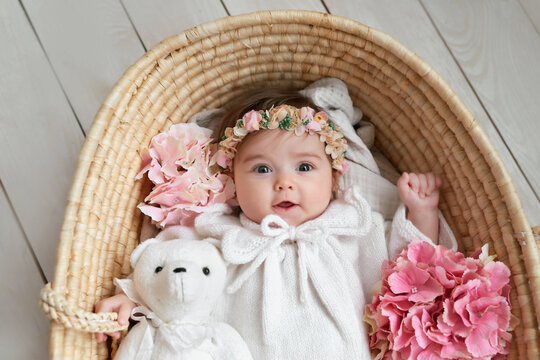 Baby girl in flower hat in wicker basket with wooden rattle. Postcard Mother's Day and Easter. Children Protection Day. World Happiness Day. Smiling child.