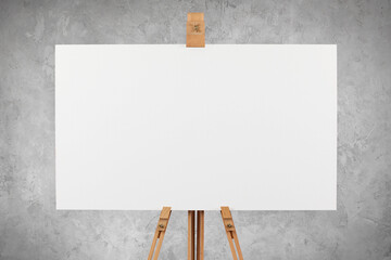 A blank artist's canvas on an easel against a concrete wall background.
 - obrazy, fototapety, plakaty