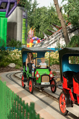 Young mother with two children in Amusement park. Family ride in small toy car. Nanny rides with children in the park.