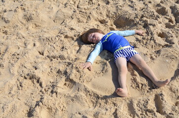 A little boy in a bathing suit lies on the sand, plays 