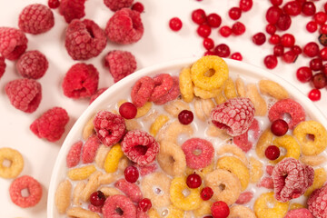 Corn rings with milk in a plate with berries and fruits, viewed from above on a white background. The concept of quick breakfast cereals