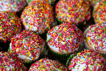 Fototapeta na wymiar Homemade cupcakes decorated sugar sprinkles in macro. Group of homemade vanilla muffins white glazed multicolored decoration. Sweet cake background