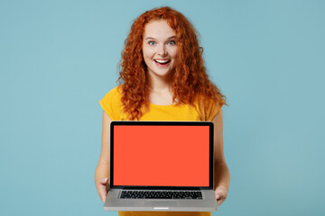 Young surprised fun happy redhead woman 20s wearing yellow t-shirt hold use work on laptop pc computer with blank screen workspace area isolated on plain light pastel blue background studio portrait