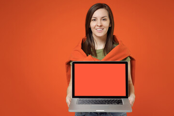 Young smiling happy woman 20s in khaki t-shirt tied sweater on shoulders hold use work on laptop pc computer with blank screen workspace area look camera isolated on plain orange background studio