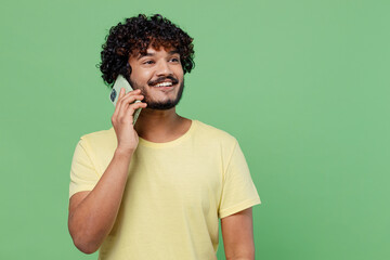 Young smiling happy Indian man 20s in basic yellow t-shirt talk speak on mobile cell phone...