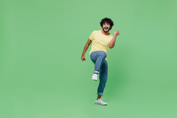 Full body young smiling Indian man 20s in basic yellow t-shirt doing winner gesture celebrate clenching fists say yes isolated on plain pastel light green background studio. People lifestyle concept.
