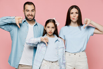 Young happy parents mom dad with child kid daughter teen girl in blue clothes showing thumb down dislike gesture isolated on plain pastel light pink background Family day parenthood childhood concept