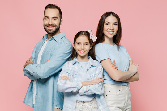 Young cheerful fun parents mom dad with child kid daughter teen girl in blue clothes hold hands crossed folded isolated on plain pastel light pink background. Family day parenthood childhood concept.