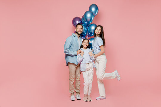 Full body young parents mom dad with child kid daughter teen girl in blue clothes celebrating birthday holiday party hold bunch inflated helium balloons hug isolated on plain pastel pink background